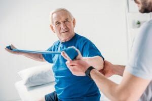 cropped shot of rehabilitation therapist assisting senior man exercising with rubber tape